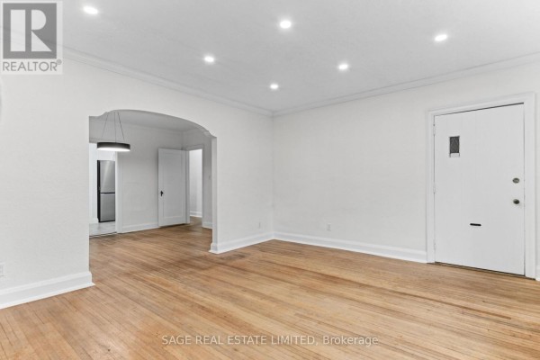 Living room with hardwood floors, an arched doorway, and a closed door on the right. - Main - 121 Braemar Avenue, Toronto