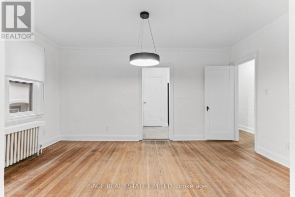 Living room with hardwood floors, a pendant light, and doorways to other rooms. - Main - 121 Braemar Avenue, Toronto