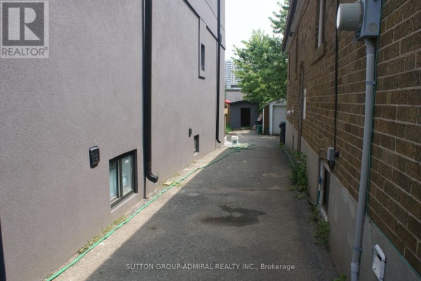 Narrow asphalt driveway between two buildings with green hoses on the ground. - Main - 131 Times Road, Toronto