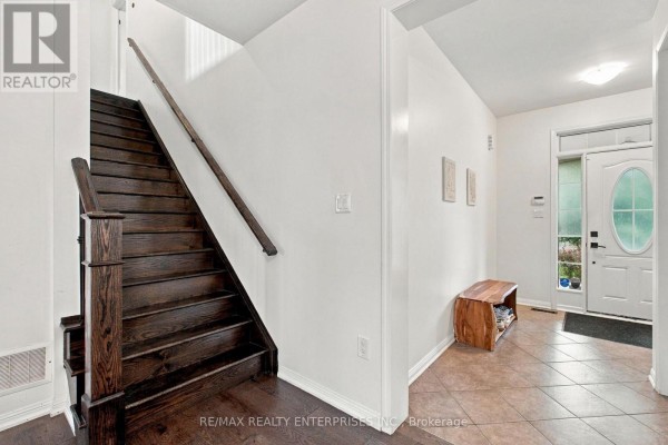 Foyer with dark wood stairs leading up, beige tile floor, and white walls. - Main - 1765 Hayden Lane, Pickering
