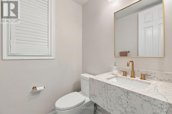 Powder room with white toilet, modern marble vanity with gold faucet, and brass toilet paper holder. - Main - 1765 Hayden Lane, Pickering