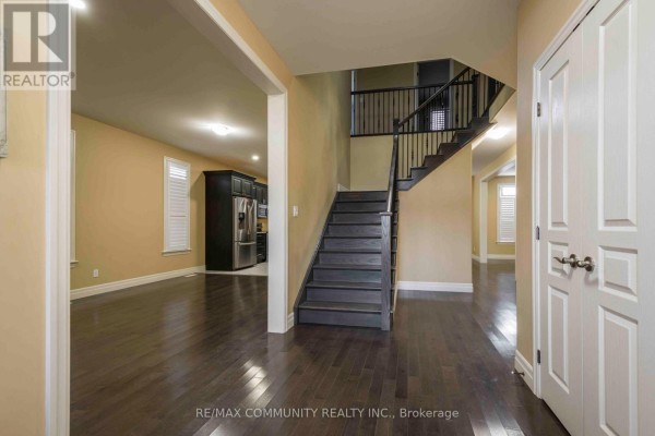 Spacious foyer with dark hardwood floors, a staircase with black railings, and views into the living area and kitchen. - Main - 19 Bevan Drive, Belleville