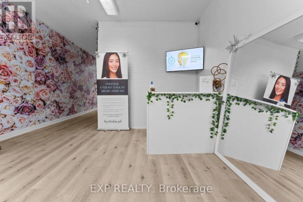 Reception desk area with floral wallpaper, digital screen, and large mirror. - Main - 213 Lakeshore Road E, Mississauga