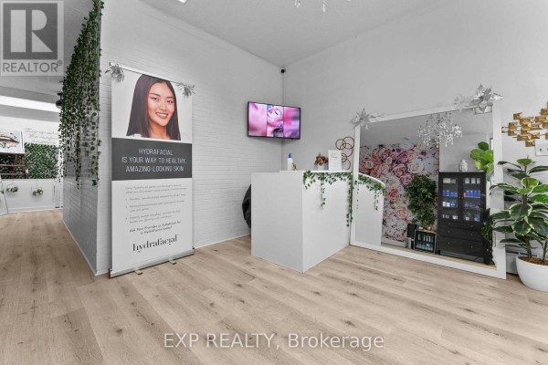 Reception desk with white counter, digital screen, large mirror, and plants. - Main - 213 Lakeshore Road E, Mississauga