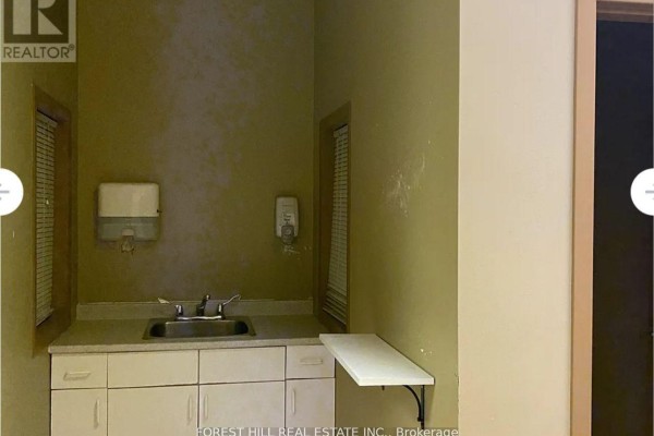 Small kitchenette area with a sink, white cabinetry, and dispensers on the wall. - Main - 257 Front Street, Belleville