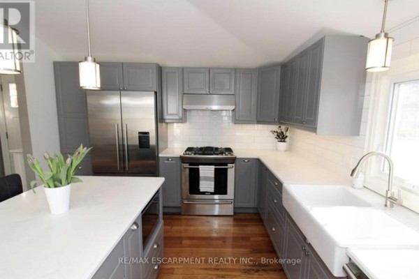 Grey kitchen cabinetry with white subway tile backsplash and a large farmhouse sink. - Main - 32 Rodman Street, St  Catharines