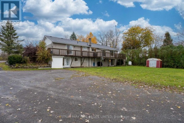 Rear exterior of a multi-unit building with a gravel driveway, grass, and a shed. - Main - 321 Rosebush Road, Quinte West
