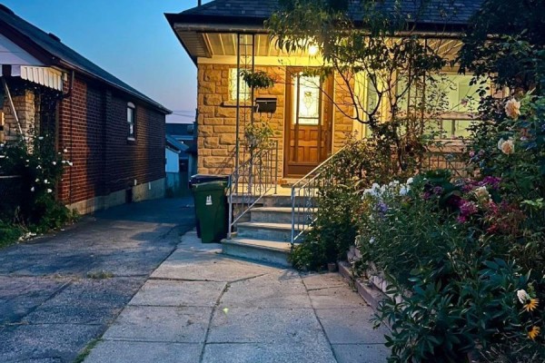Exterior of a stone bungalow with a driveway and garden at dusk. - Main - 354 Kane Avenue, Toronto