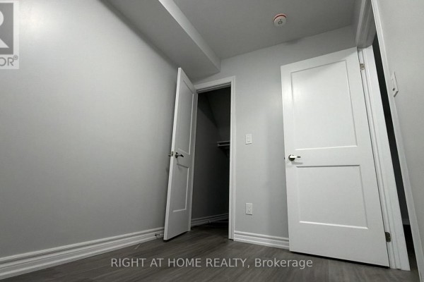 Empty room with light grey walls, dark laminate flooring, and two doors, one open to a closet. - Main - 408 Strathmore Boulevard, Toronto