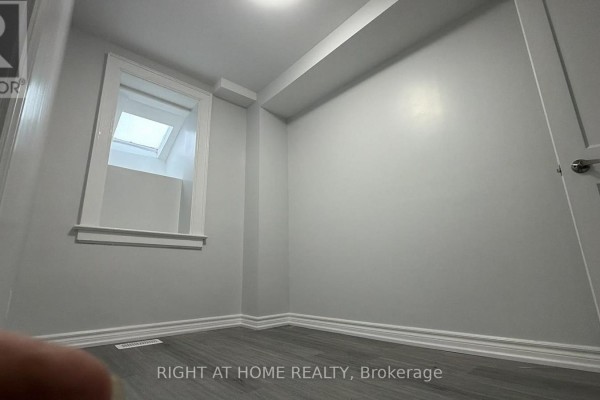 Empty room with light grey walls, dark laminate flooring, and a skylight window. - Main - 408 Strathmore Boulevard, Toronto