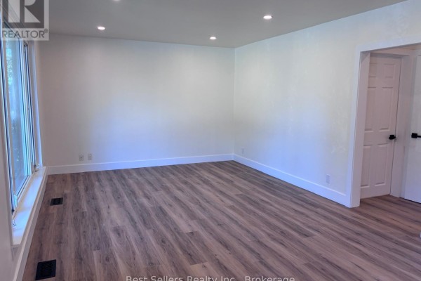 Living room with light walls, wood-look vinyl flooring, and a large window. - Main - 767 Gaspe Avenue, Oshawa