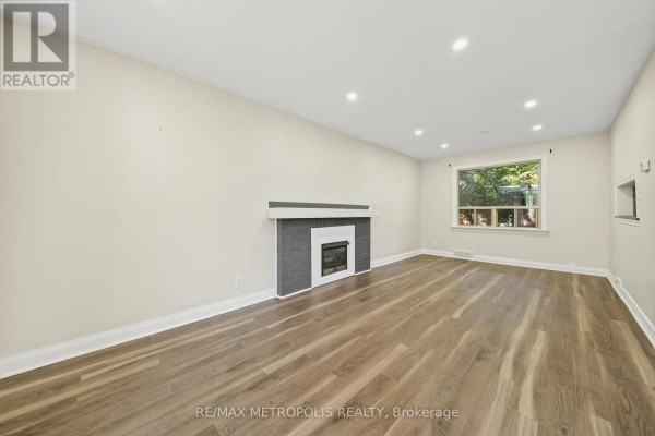 Living room with a gray and white fireplace, light wood laminate flooring, and recessed lighting. - Main - 78 Harold Street, Brampton