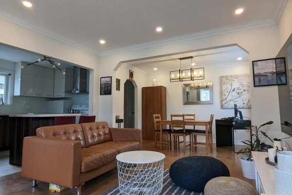 Open concept living, dining, and kitchen area with brown leather sofa and wooden dining set. - Main - 85 Ranstone Gardens, Toronto