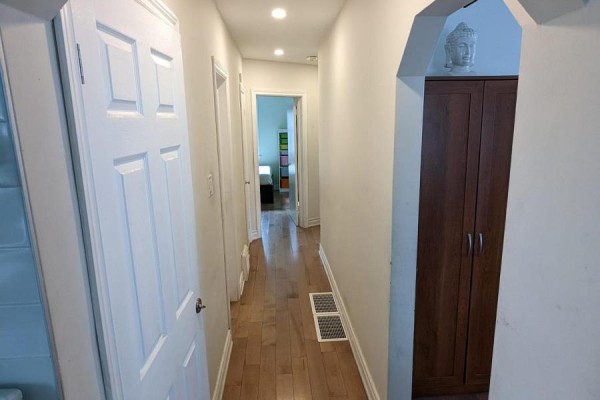 Hallway with light wood floors, white doors, and a tall dark wood cabinet on the right. - Main - 85 Ranstone Gardens, Toronto