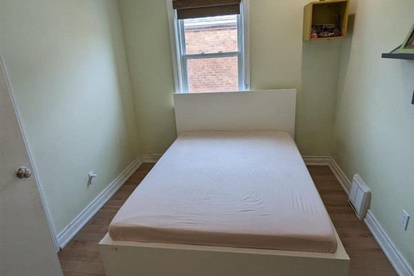 Small bedroom with a white bed frame, light green walls, and a window with brick building view. - Main - 85 Ranstone Gardens, Toronto