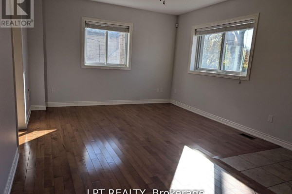 Bedroom with hardwood floors, beige walls, and two windows offering views of the exterior. - Main - 9 Atkinson Avenue, Toronto