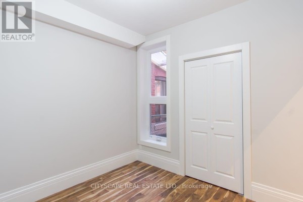 Empty room with white bi-fold closet doors, a tall narrow window, and hardwood floors. - Main - 936 Dundas Street E, Toronto