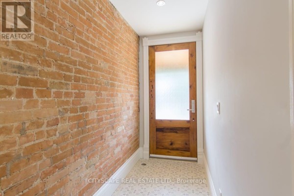 Entrance hallway with exposed brick wall, tiled floor, and a rustic wooden door with frosted glass. - Main - 936 Dundas Street E, Toronto