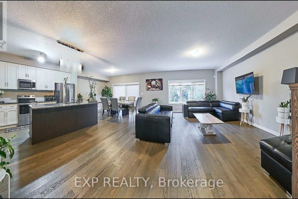 Open-concept living and dining area with hardwood floors, a large sectional sofa, dining table, and a television. - Main - 967 Wright Drive, Midland