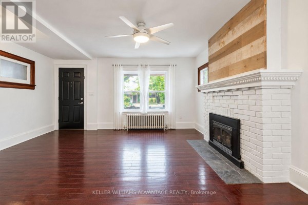 Living room with fireplace, white brick surround, gas insert, and dark hardwood floors. - Main & 2nd - 585 Woodbine Avenue, Toronto