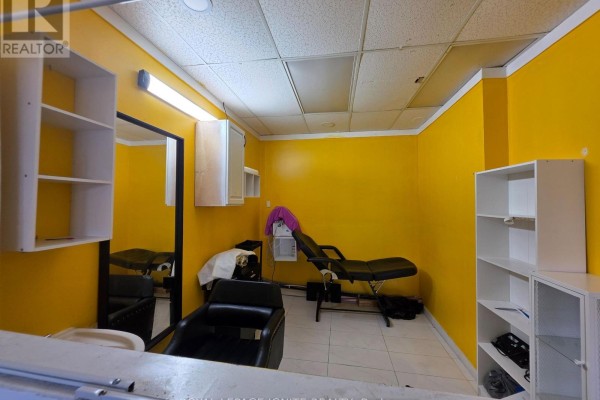 Another view of the yellow room with shelves, a styling chair, a massage table, and white storage units. - Main Floor (front Side) - 2426 Kingston Road, Toronto