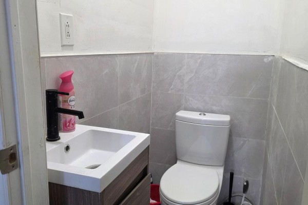 A small washroom with a white toilet and a vanity sink with a black faucet against grey tiled walls. - Main Floor (front Side) - 2426 Kingston Road, Toronto