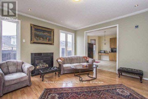 Living room with a fireplace, sofa, armchair, and a view into the kitchen. - Main Floor - 11 Horsetail Street, Markham
