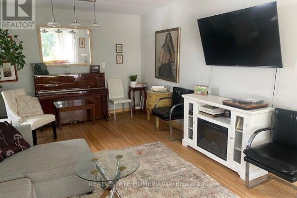 Living room with a brown upright piano, a television, and a sectional sofa. - Main Floor - 1407 Kenmuir Avenue, Mississauga