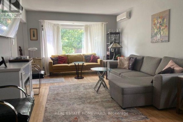 Living room with a large bay window, a yellow sofa, and a grey sectional. - Main Floor - 1407 Kenmuir Avenue, Mississauga