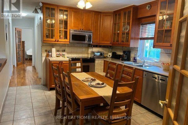 Kitchen with wooden cabinets, tiled floor, stainless steel appliances, and a wooden dining table. - Main Floor - 15 Lynnhaven Road, Toronto