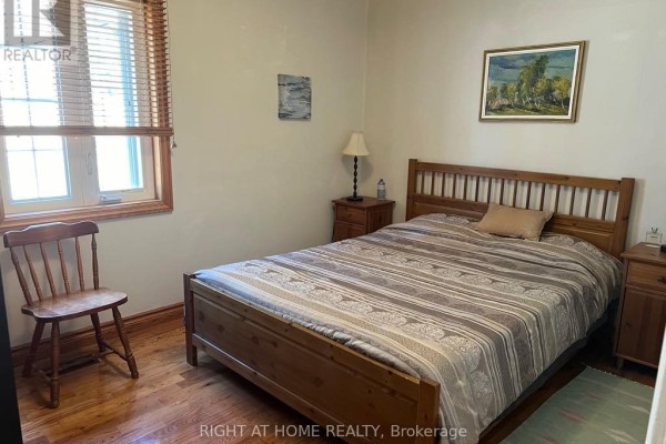 Bedroom with a wooden bed frame, striped bedding, hardwood floors, and a wooden chair. - Main Floor - 15 Lynnhaven Road, Toronto