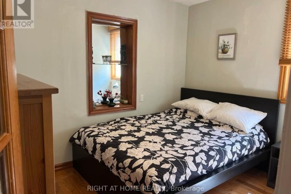Bedroom with a dark bed frame, floral bedding, hardwood floors, and a recessed display shelf. - Main Floor - 15 Lynnhaven Road, Toronto