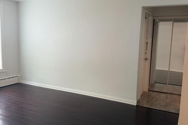 Interior view of a room with dark hardwood floors, white walls, and a mirrored closet door. - Main Floor - 2 Rowley Avenue, Toronto