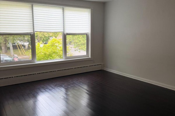 Living room with dark hardwood floors, white pleated blinds covering three windows, and white walls. - Main Floor - 2 Rowley Avenue, Toronto