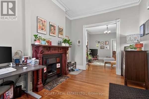 Living room with a dark wood fireplace, desk, and opening to a dining area. - Main Floor - 20 Draper Street, Toronto