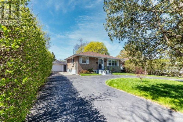 Side exterior view of a brick bungalow with a detached garage and driveway. - Main Floor Apartment - 438 Third Line, Oakville