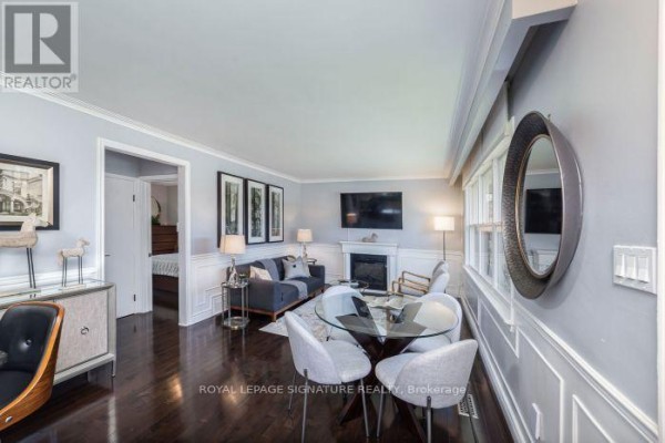 Living room with a fireplace, grey sofa, glass dining table, and dark hardwood floors. - Main Floor Apartment - 438 Third Line, Oakville