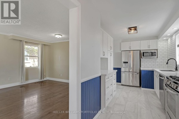 Open concept living room and kitchen with hardwood floors, white cabinets, stainless steel appliances, and blue wainscoting. - Main Flr - 1519 Lakeside Street, Oshawa
