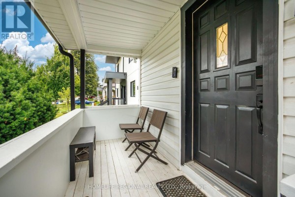 Covered front porch with seating area, dark brown front door, and white railing. - Main Level - 21 Acorn Avenue, Toronto