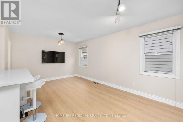 Living area with light wood floors, white island with stools, and television. - Main Level - 21 Acorn Avenue, Toronto