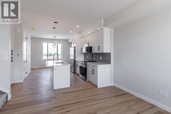 Kitchen with white cabinets, grey backsplash, stainless steel appliances, and island. - Mccaskill Drive #1931, Crossfield