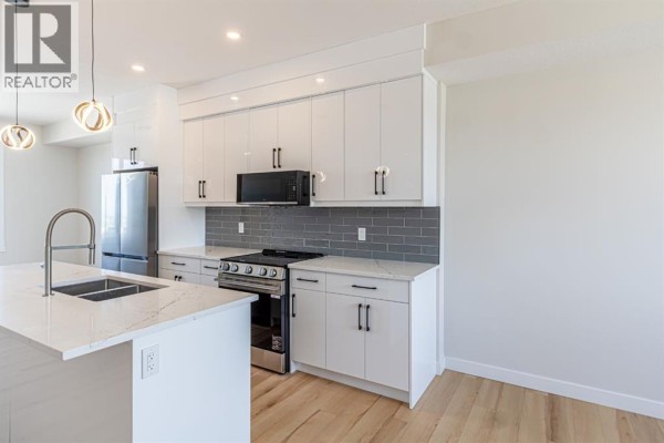 Close-up of kitchen with white island, stainless steel range, microwave, and cabinets. - Mccaskill Drive #1931, Crossfield
