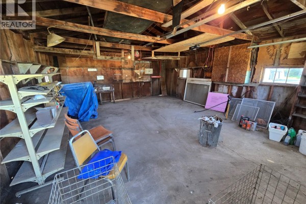 Interior of a rustic garage with concrete floor, exposed wood walls, and storage shelves. - Mccormick Acreage, Weyburn Rm No  67