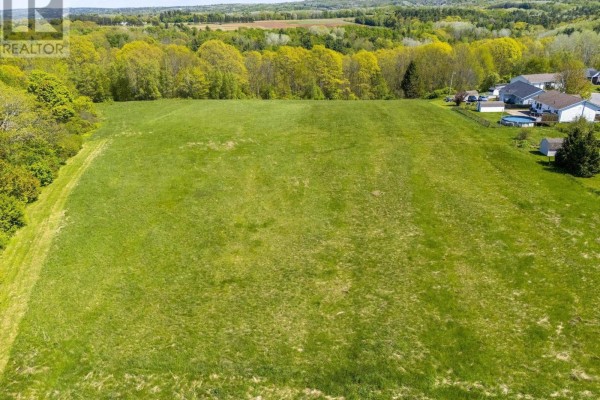 View of a grassy area bordered by trees, with homes visible in the background. - Mill Run Extension Extension, Kentville
