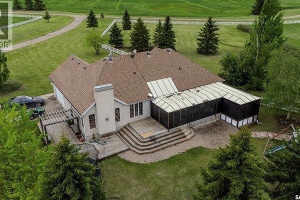 Side aerial view of the beige house showing the extensive roofline and adjacent white fencing. - Misty Lane Acreage, Orkney Rm No  244