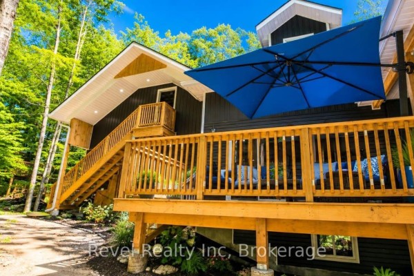 Wooden deck with railings and a large blue umbrella overlooks a wooded backyard area. - 157 Desroches Trail, Tiny
