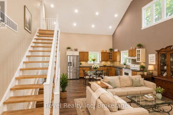 Open concept living room and kitchen with vaulted ceiling, wood staircase, sofas, dining table, and hutch - 157 Desroches Trail Tiny