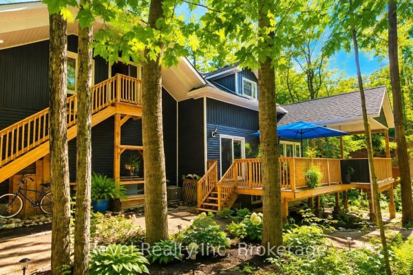 Dark siding home with wooden deck, stairs, bicycle, and blue umbrella - 157 Desroches Trail Tiny