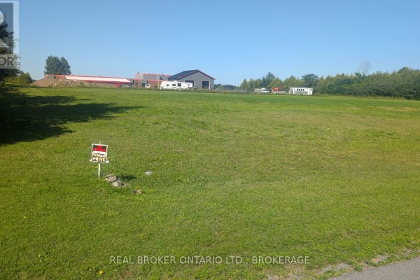 Green field with a white marker post and a large building with a red roof in the background. - N/a Florence Street, North Glengarry