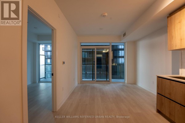 Living area with light wood floors, white walls, and balcony doors overlooking a city building. - N1301 - 117 Broadway Avenue N, Toronto